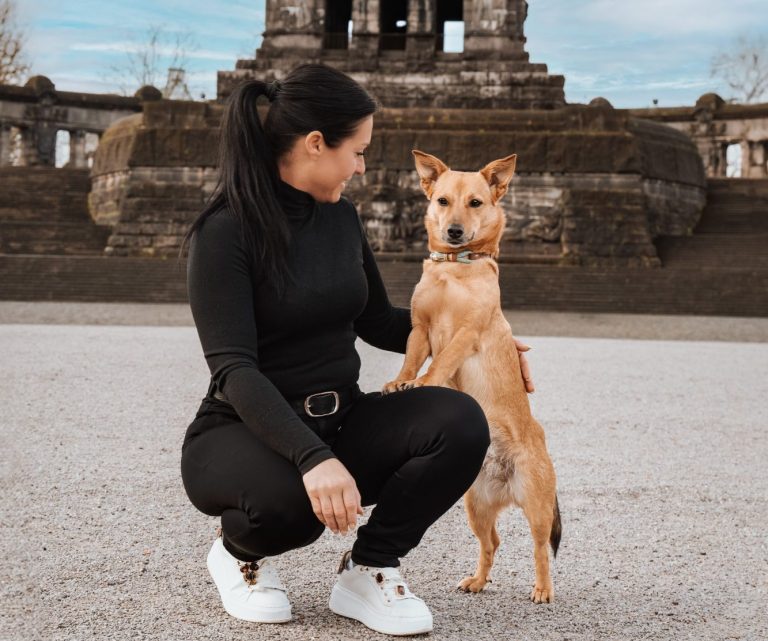 Eine Frau kniet neben einem stehenden Hund vor einer historischen Statue.