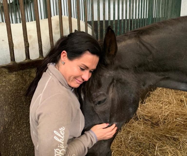 Frau umarmt ein Pferd in einer Stallumgebung, umgeben von Stroh.